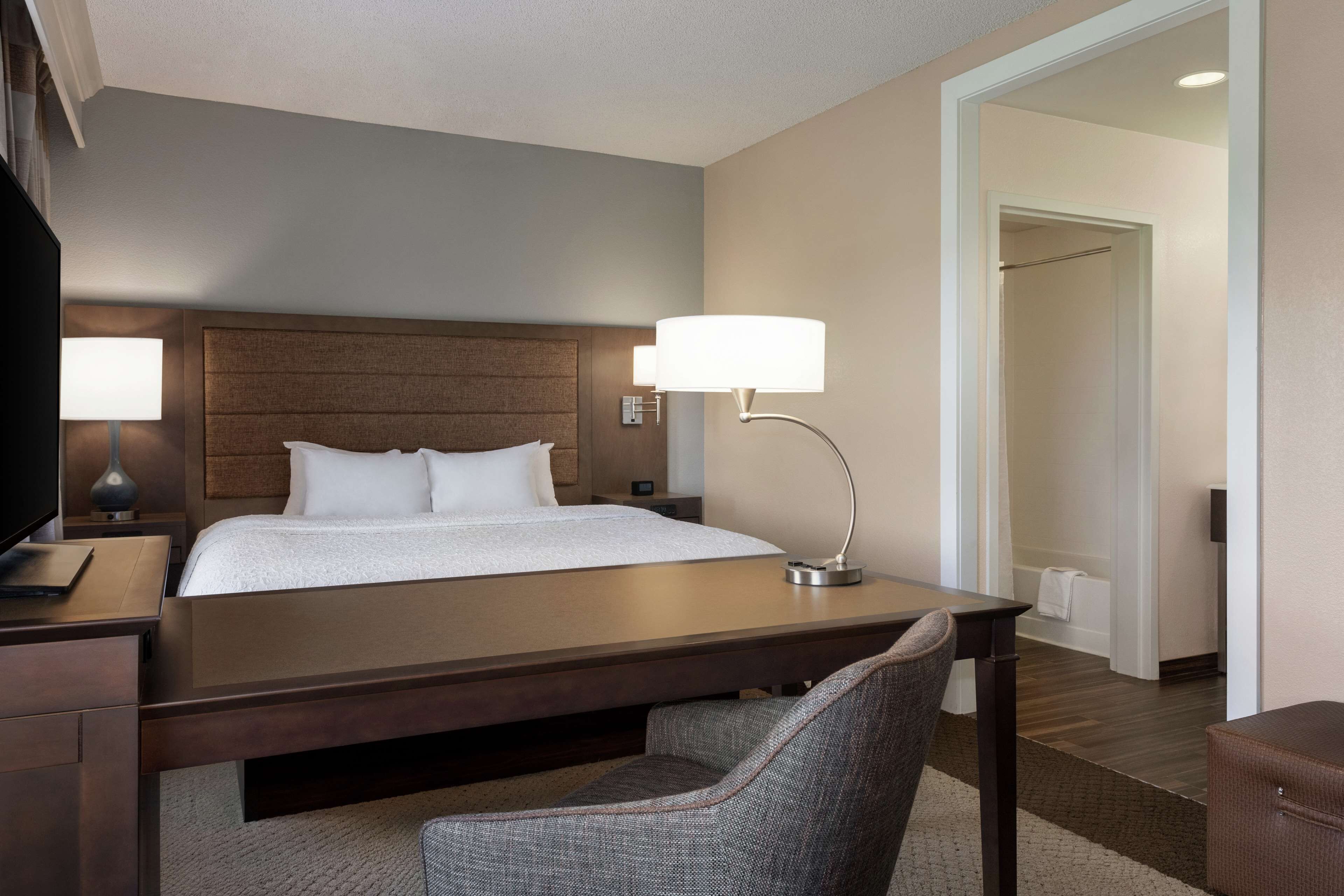 A hotel room with a bed, bedside lamps, a desk, and a chair.