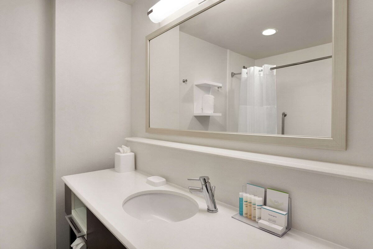 A modern bathroom with a white sink, a mirror, and a shower curtain.