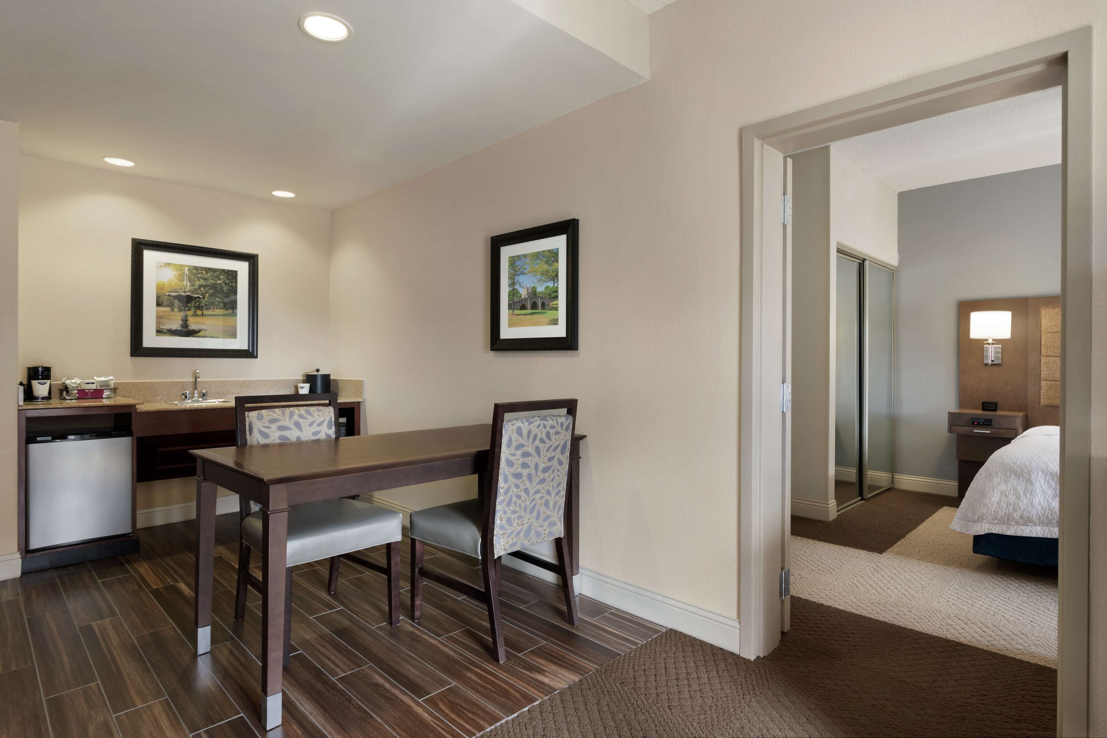 Habitación de hotel con cama, mesita de noche, lámpara, espejo y baño visible a través de una puerta abierta.