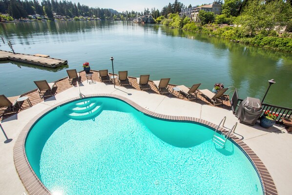 A swimming pool with a deck, lounge chairs, and a view of a lake. - Lakeshore Inn (Lake Oswego)