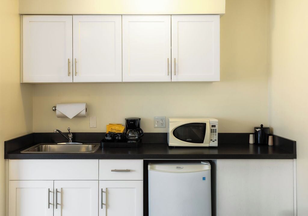 Una cucina con mobili bianchi, un piano di lavoro nero, un lavello in acciaio inossidabile, un forno a microonde, una macchina da caffè e una lavastoviglie.