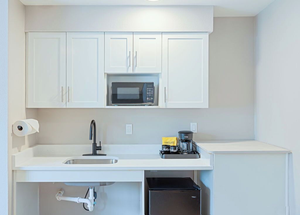 A kitchen with white cabinets, a microwave, a coffee maker, and a black refrigerator.