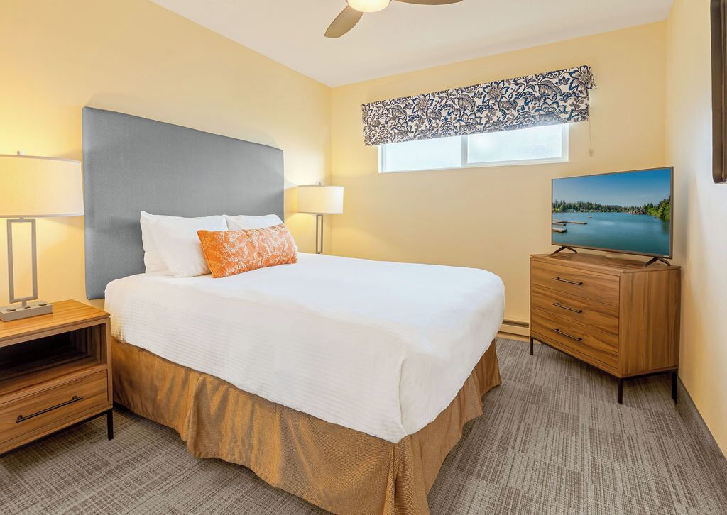 A hotel room with a bed, bedside tables, a TV, and a window with a view.