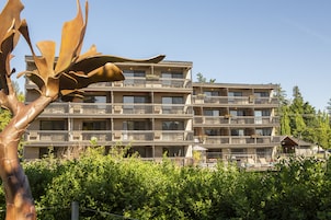 Un hotel de varios pisos con balcones, piscina y abundante vegetación en primer plano.