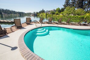 A swimming pool with a clear blue center, surrounded by lounge chairs and a wooden deck.