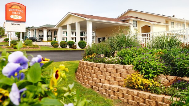 A Whispering Hills Inn with a large sign, multiple balconies, and a landscaped garden with various plants. - Whispering Hills Inn (Branson)