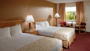A hotel room with two beds, a small table, a chair, and a window with curtains. - Whispering Hills Inn (Branson)