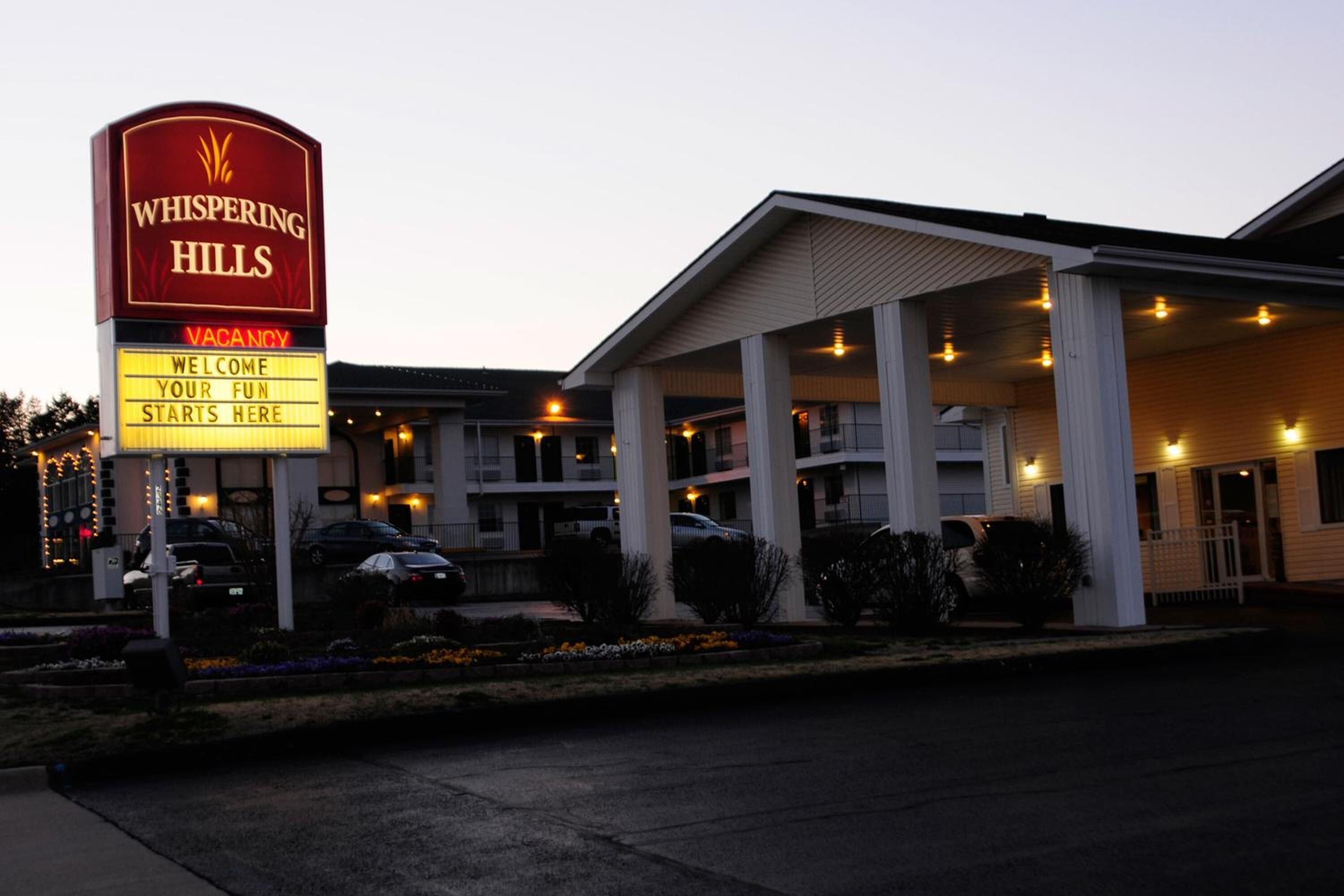 A hotel named Whispering Hills with a signboard indicating vacancy and welcoming guests.