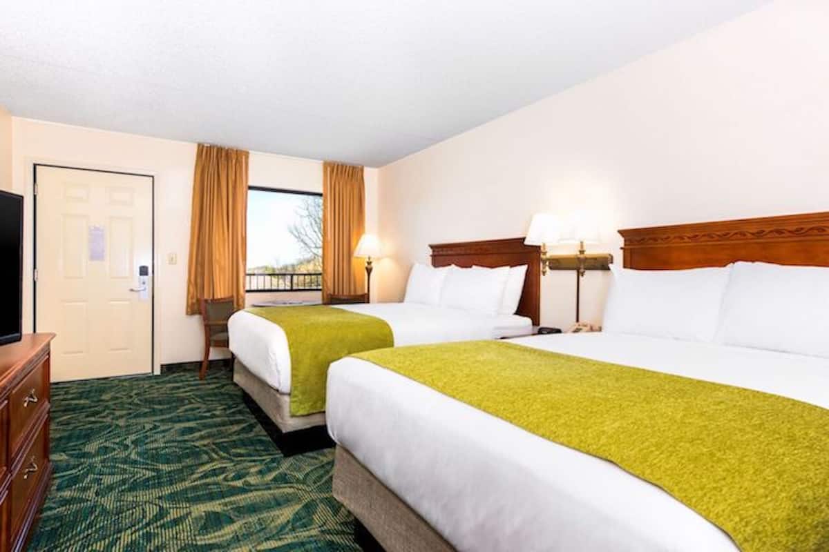 A hotel room with two beds, a television, a desk, and a window with curtains.