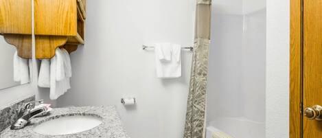 A bathroom with a granite sink, wooden cabinet, white towels, and a shower with a beige curtain.