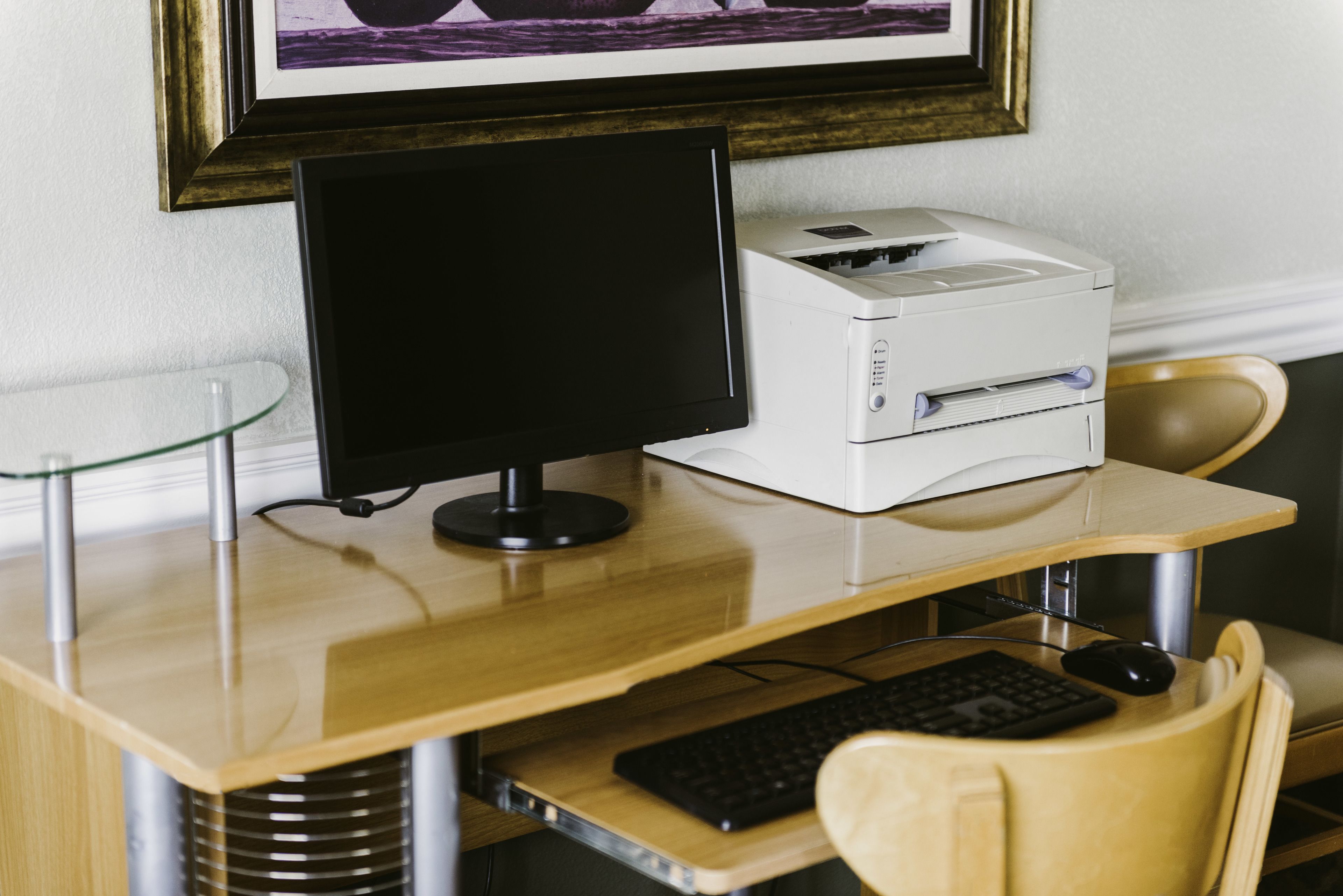 A computer desk with a monitor, printer, keyboard, and mouse.
