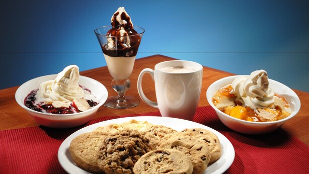 Una mesa de postres con helados en recipientes, una taza y galletas.