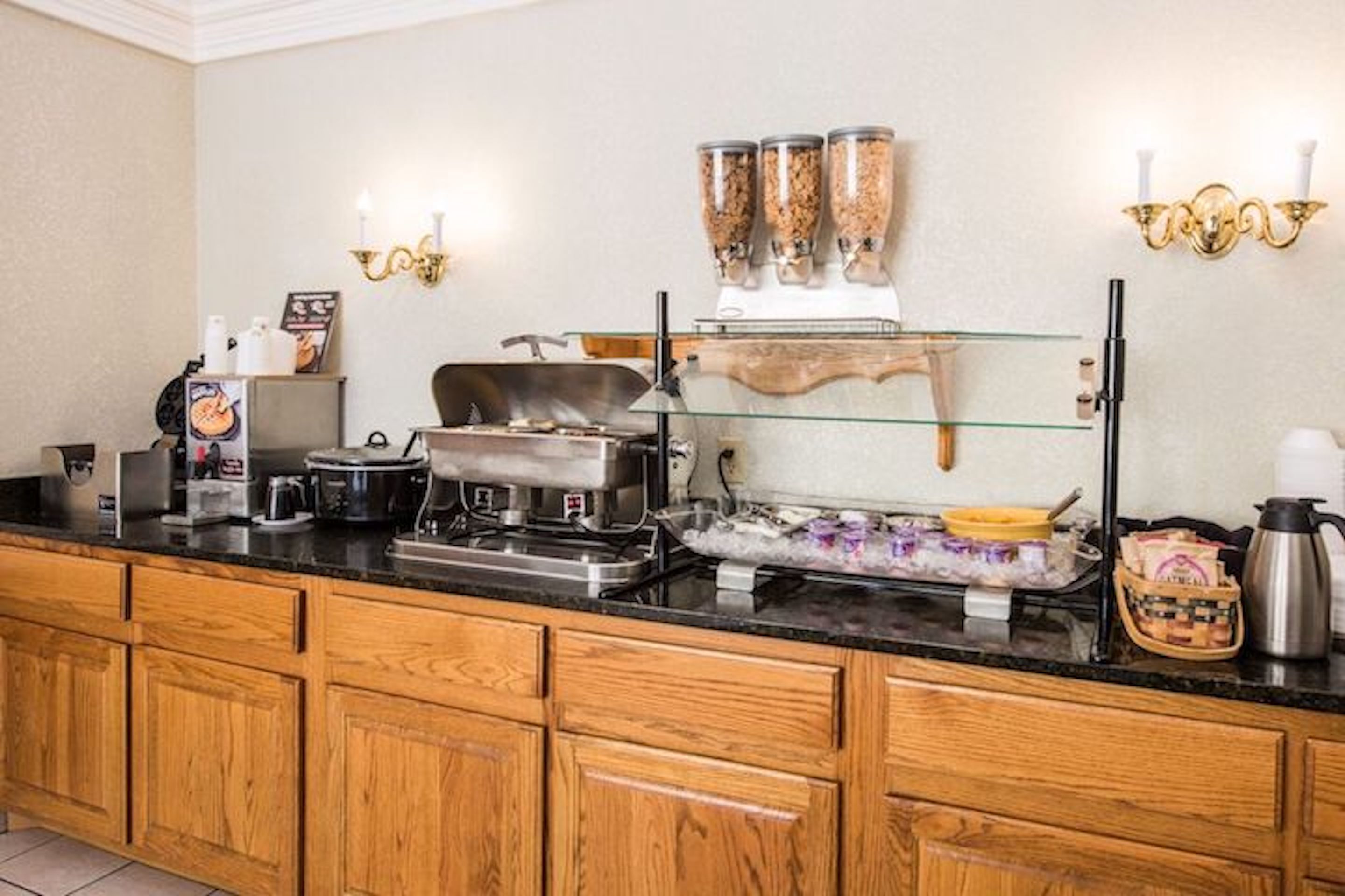 Disposição de buffet com uma vitrine de vidro, uma máquina de café e uma chaleira em um balcão de madeira.