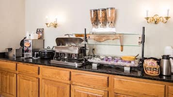 Disposição de buffet com uma vitrine de vidro, uma máquina de café e uma chaleira em um balcão de madeira.