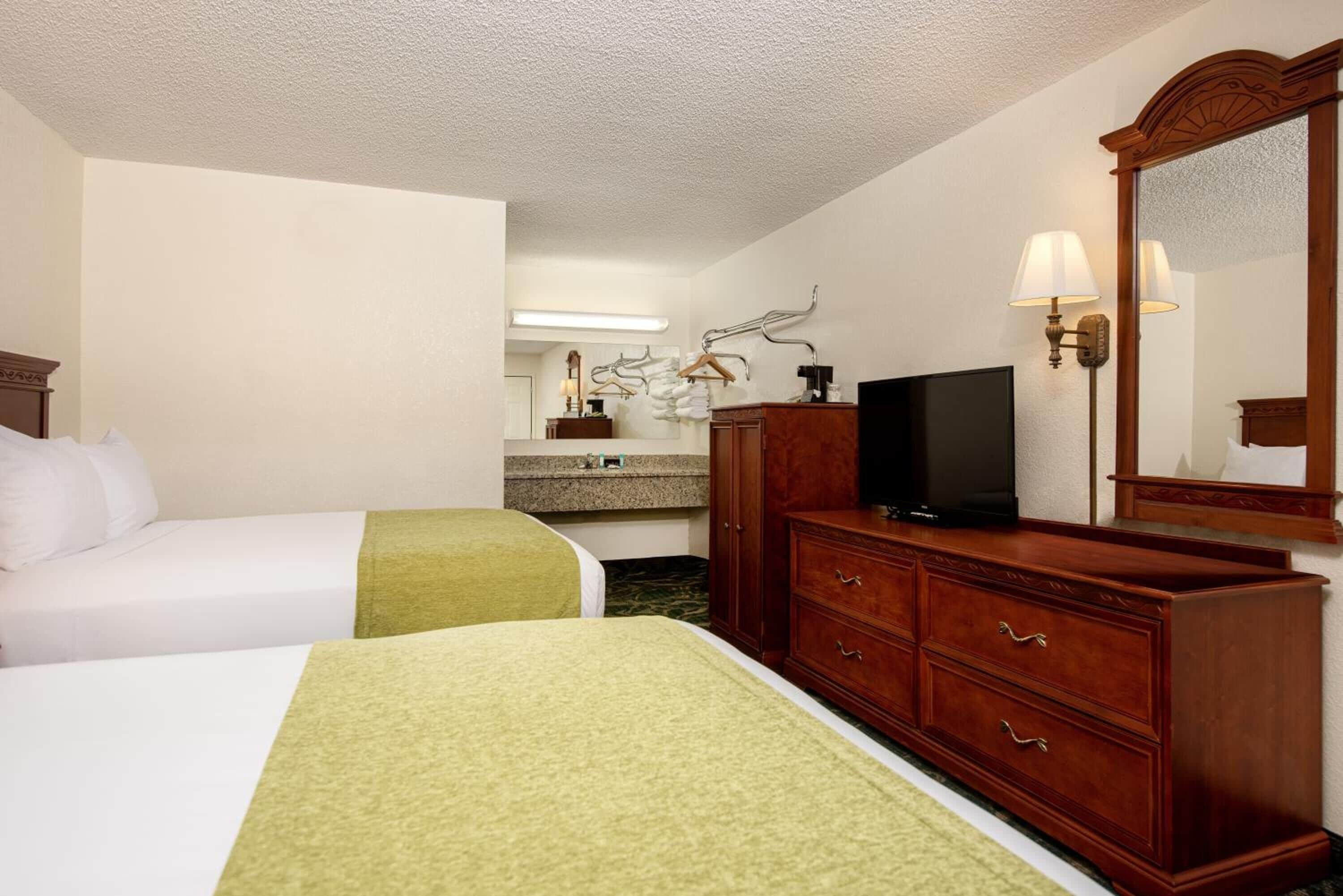 Una habitación de hotel con dos camas, un aparador, un televisor y un espejo.