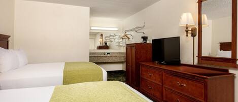 Una habitación de hotel con dos camas, un aparador, un televisor y un espejo.