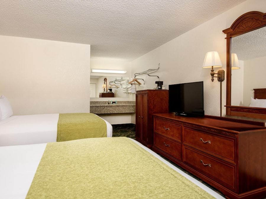 A hotel room with two beds, a dresser, a television, and a mirror.