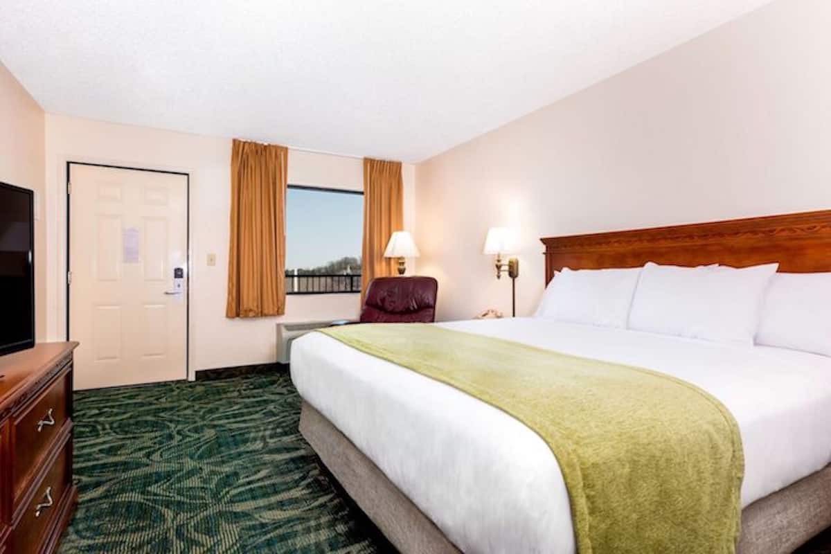 A hotel room with a bed, a television, a desk, and a window with curtains.