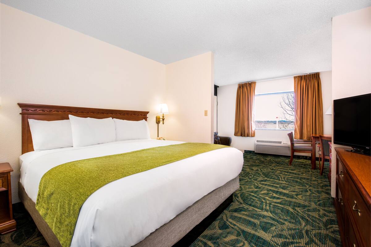 A hotel room with a large bed, a desk, a television, and a window with curtains.