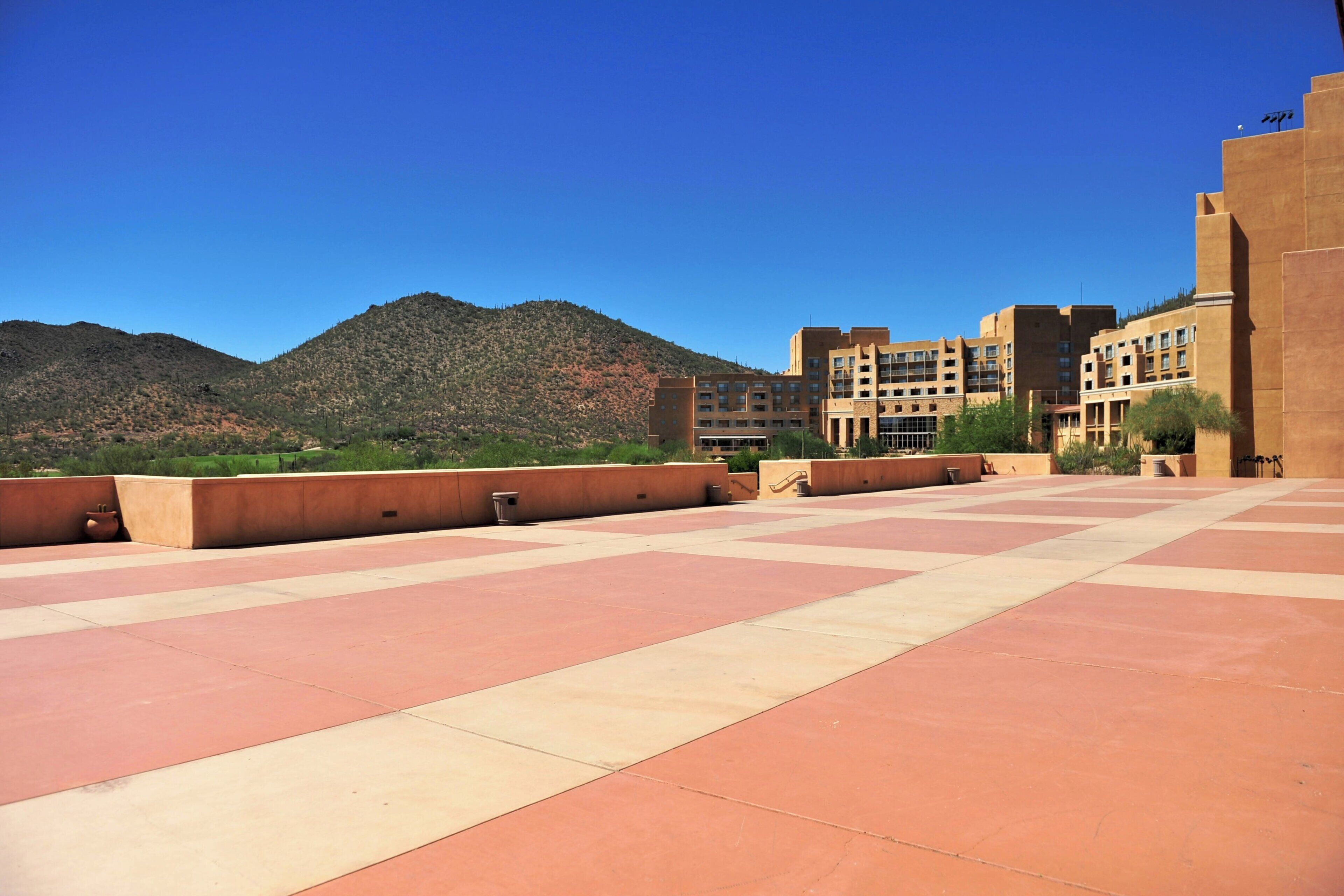A courtyard with a tiled floor, a building with multiple floors, and a mountain in the background.