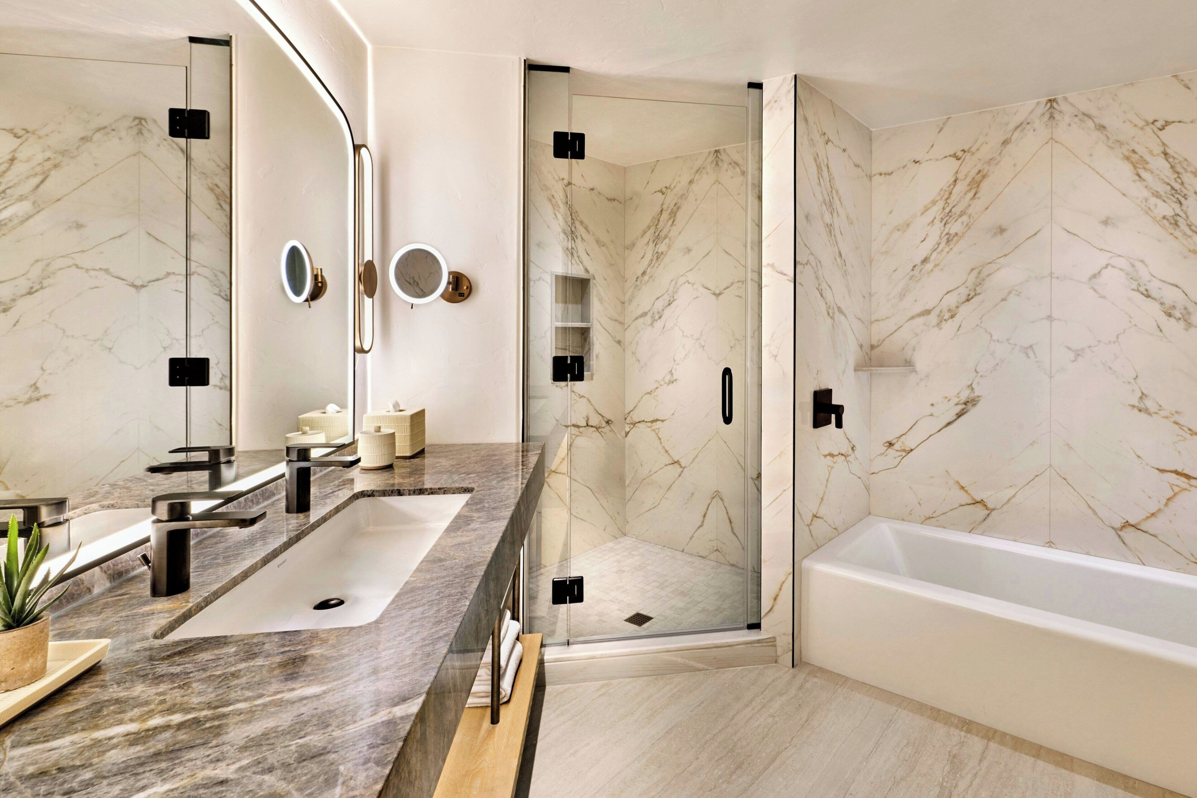 A modern bathroom with a marble vanity, a bathtub, and a glass-enclosed shower.