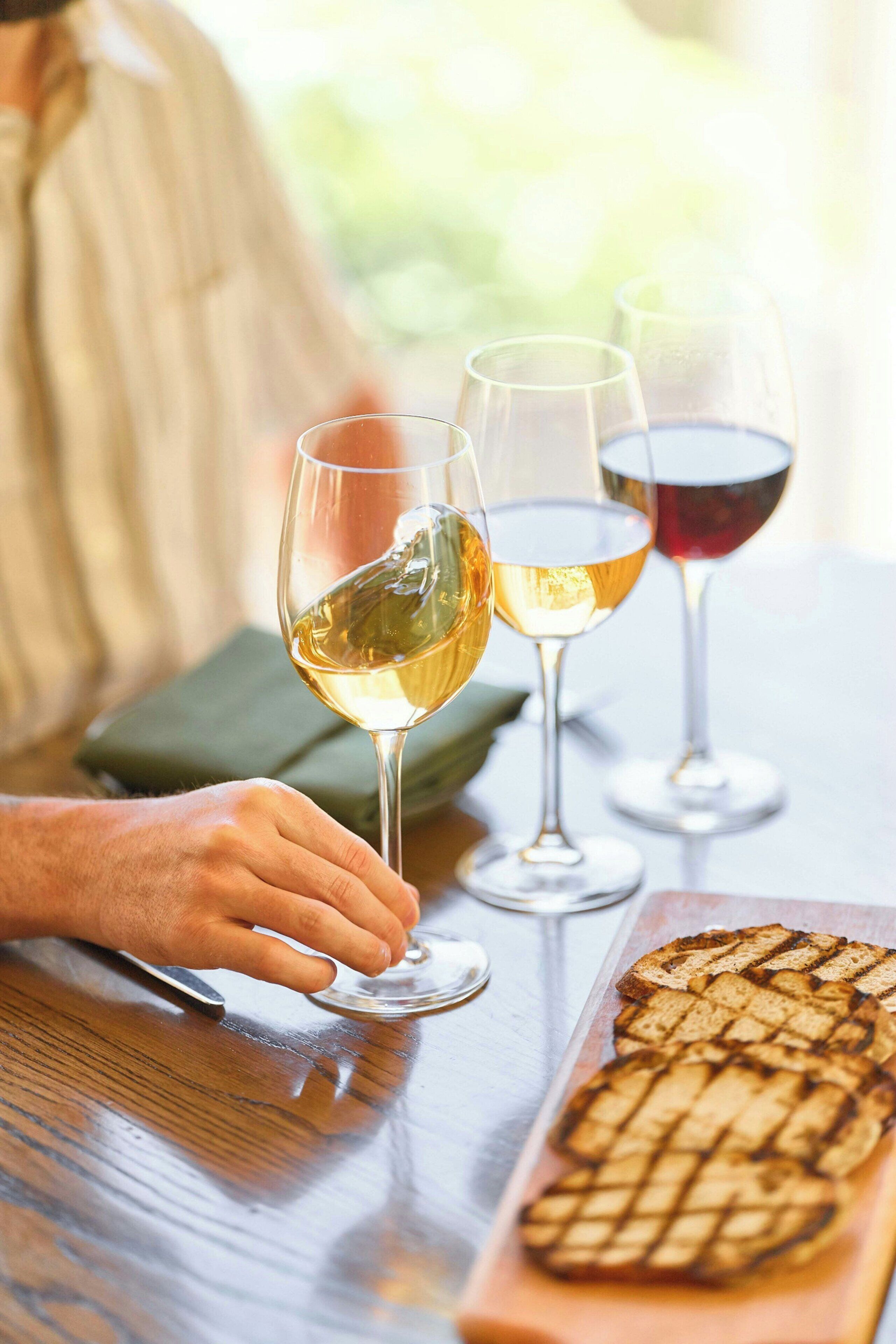 A person holding a wine glass, with two other wine glasses on the table.