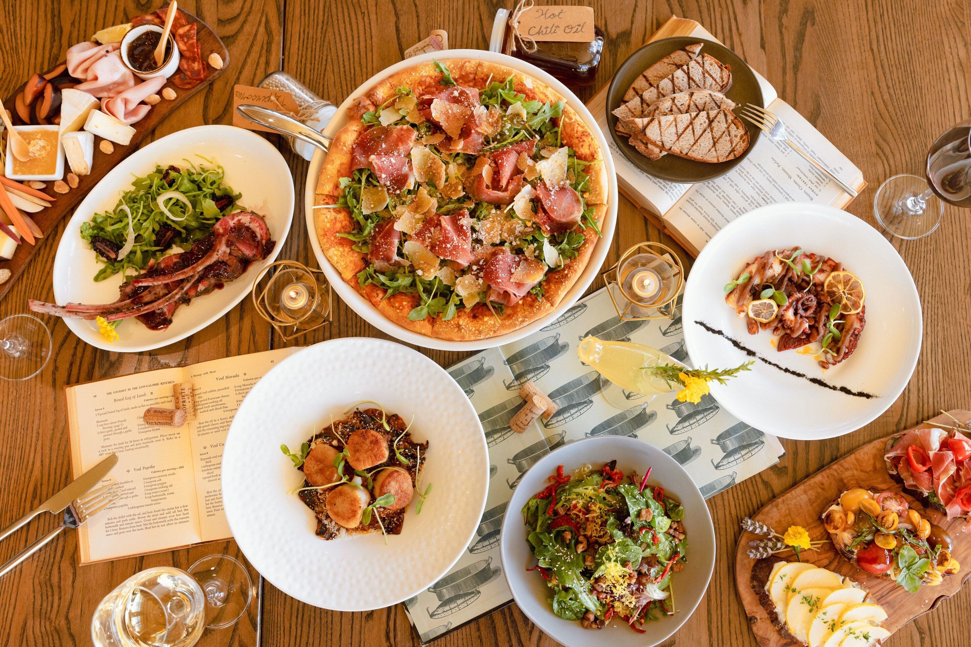 A variety of dishes including a pizza, salads, and appetizers, suggesting a restaurant setting.