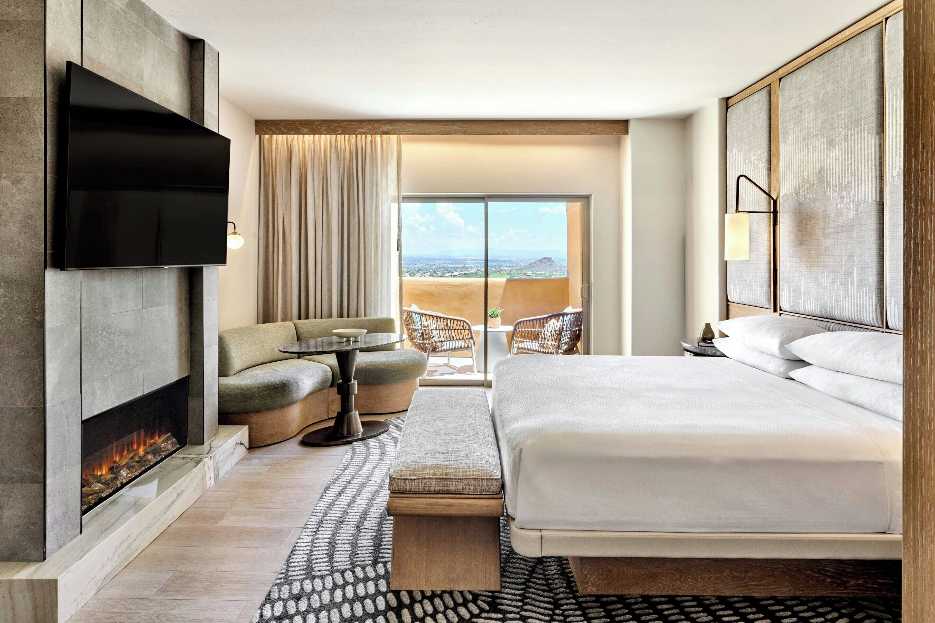 Une chambre d’hôtel moderne dotée d’une cheminée, d’un grand lit, d’un canapé, d’une table à manger et d’un balcon avec vue.