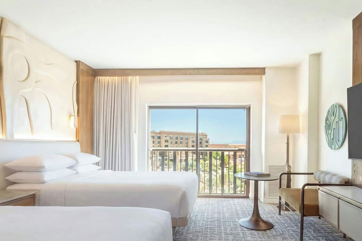 A hotel room with two beds, a balcony, a small table, and a TV.