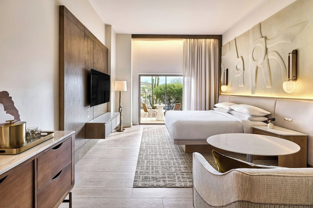 A hotel room with a large bed, a TV, a bedside table, a chair, and a view of the outdoors.