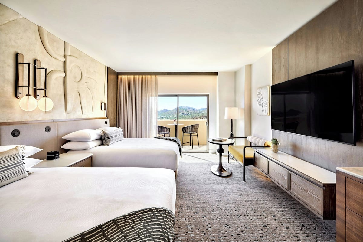 A hotel room with two beds, a large TV, a desk, and a view of the mountains.