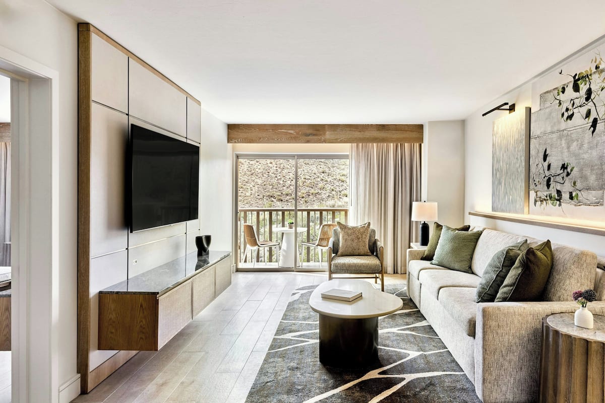 A modern living room with a flat-screen TV, a sofa, a coffee table, and a balcony with outdoor seating.