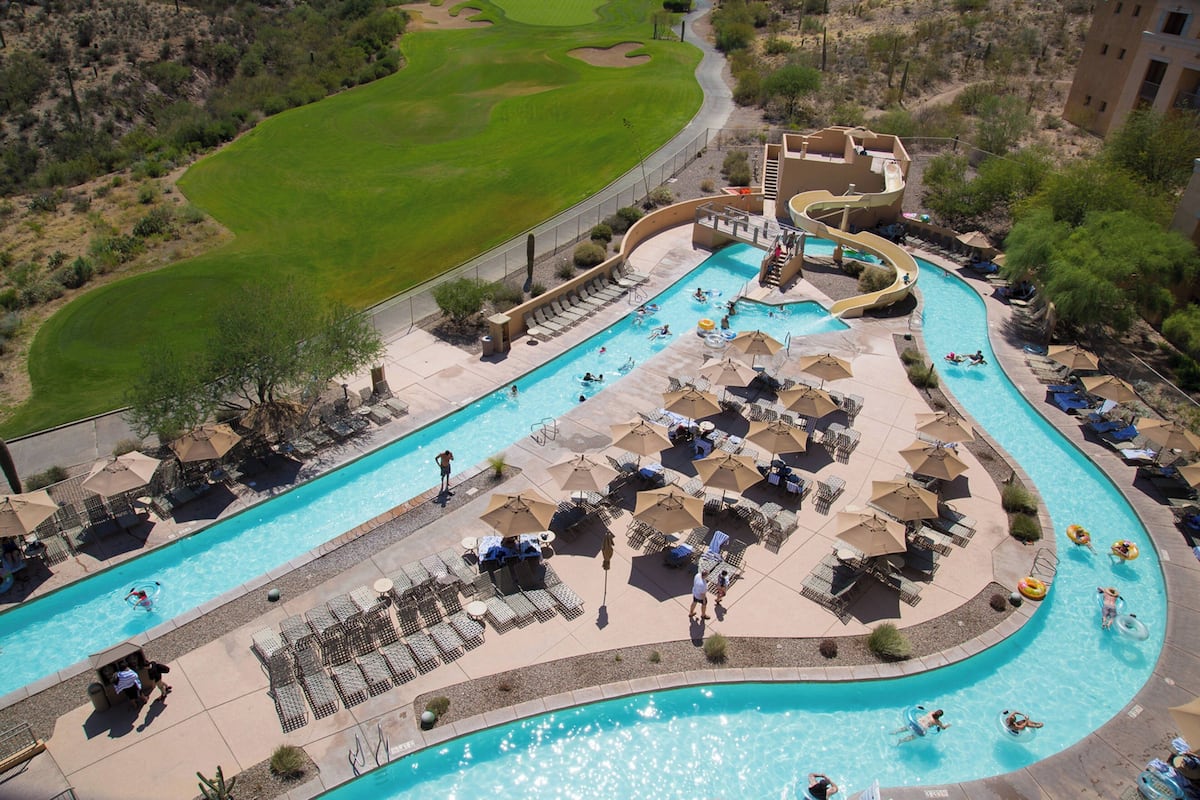 A swimming pool with a water slide, lounge chairs, and umbrellas.