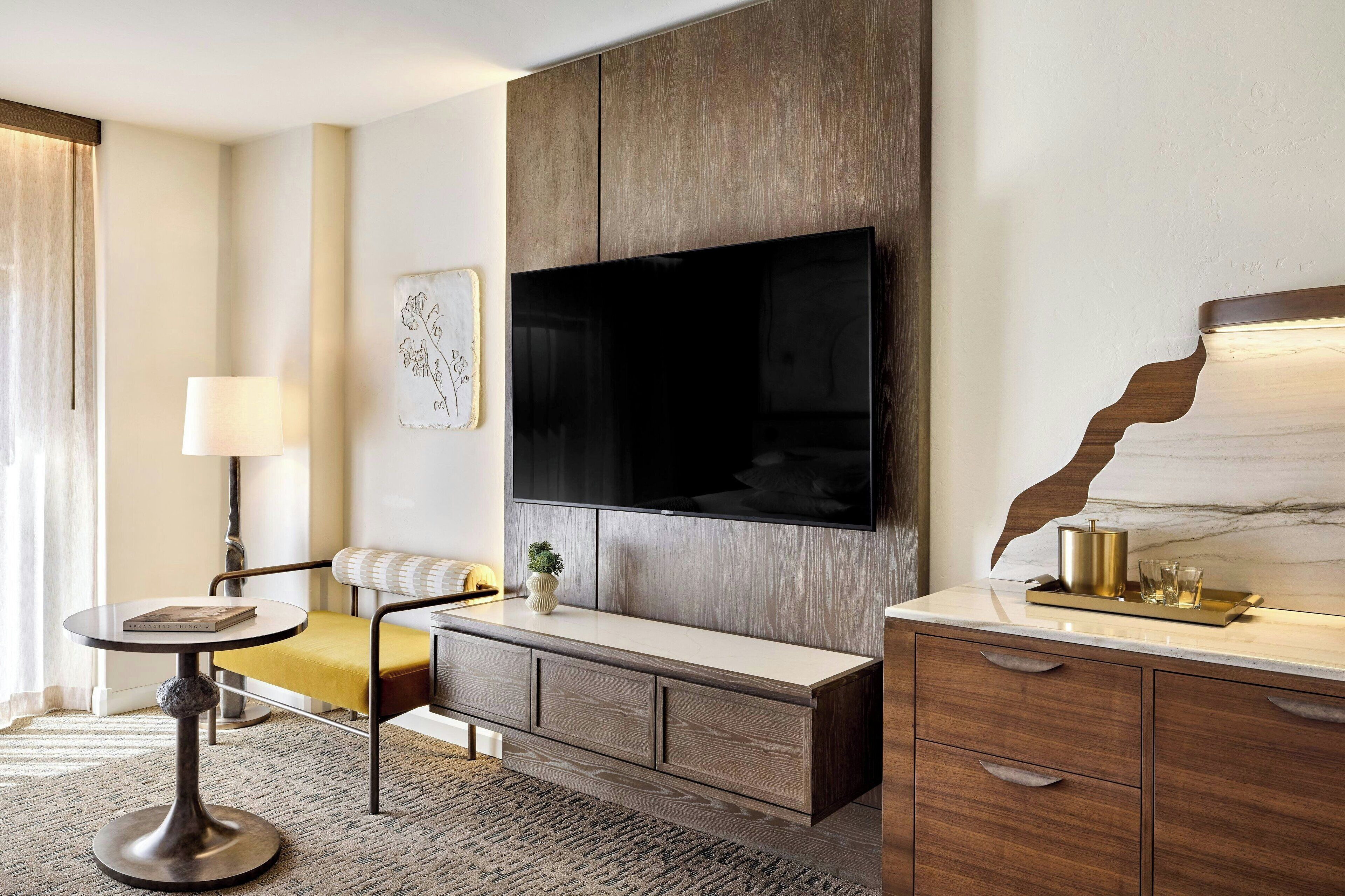 A modern living room with a large flat-screen TV mounted on a wooden wall, a sofa, a small round table with a lamp, and a decorative plant.