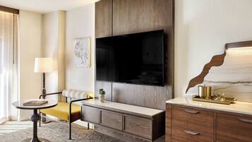 A modern living room with a large flat-screen TV mounted on a wooden wall, a sofa, a small round table with a lamp, and a decorative plant.