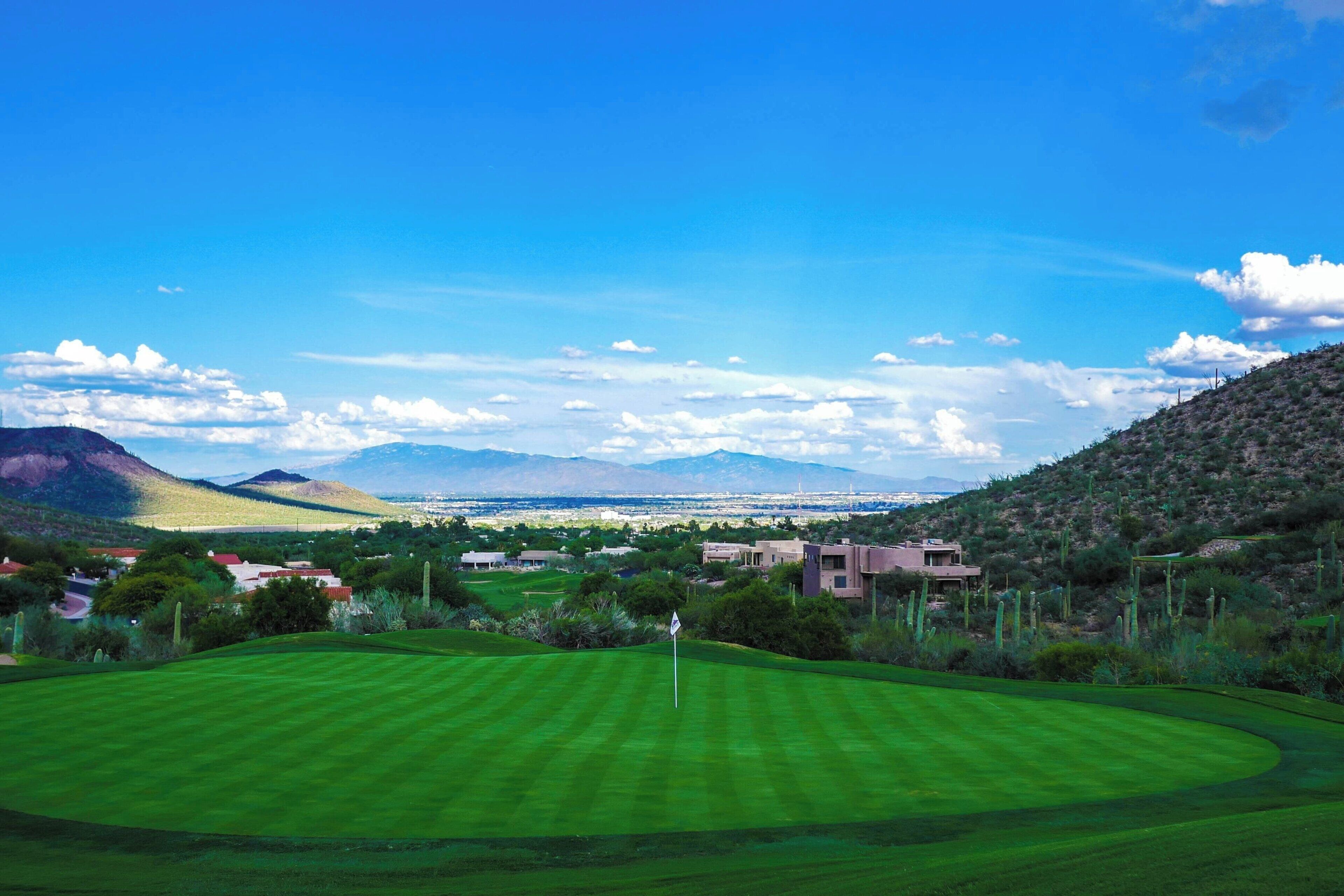 Un campo de golf con vistas despejadas a montañas lejanas y un paisaje urbano.