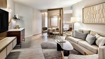 A modern living room with a sofa, coffee table, and a TV. There is a dining area with a table and chairs. The room has a neutral color palette and wooden flooring.