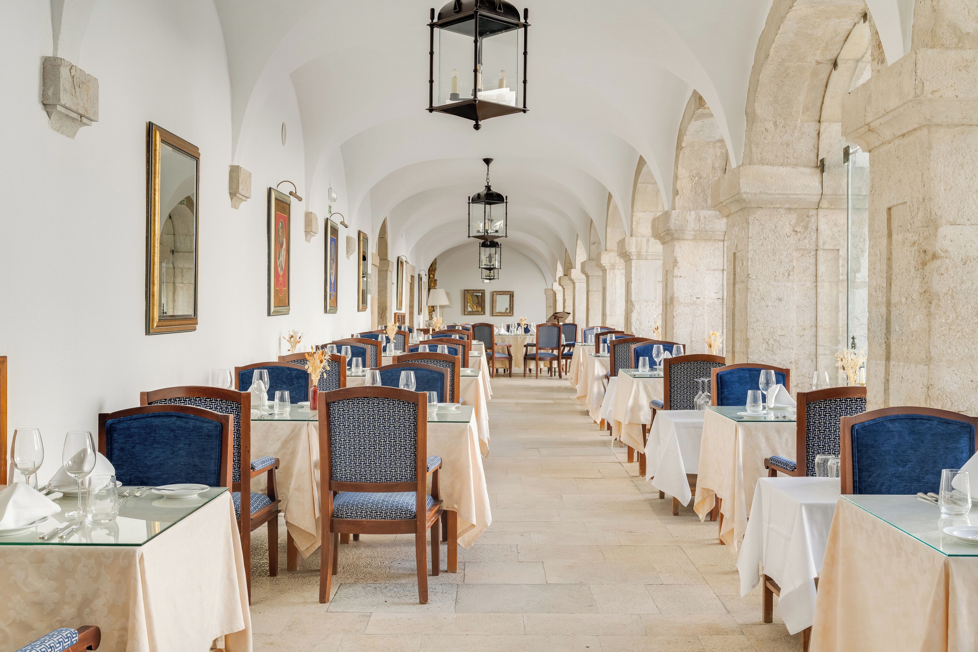 A long dining hall with tables and chairs, arched ceilings, and hanging lanterns.