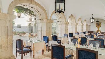 An indoor dining area with stone arches, glass tables, and blue upholstered chairs.