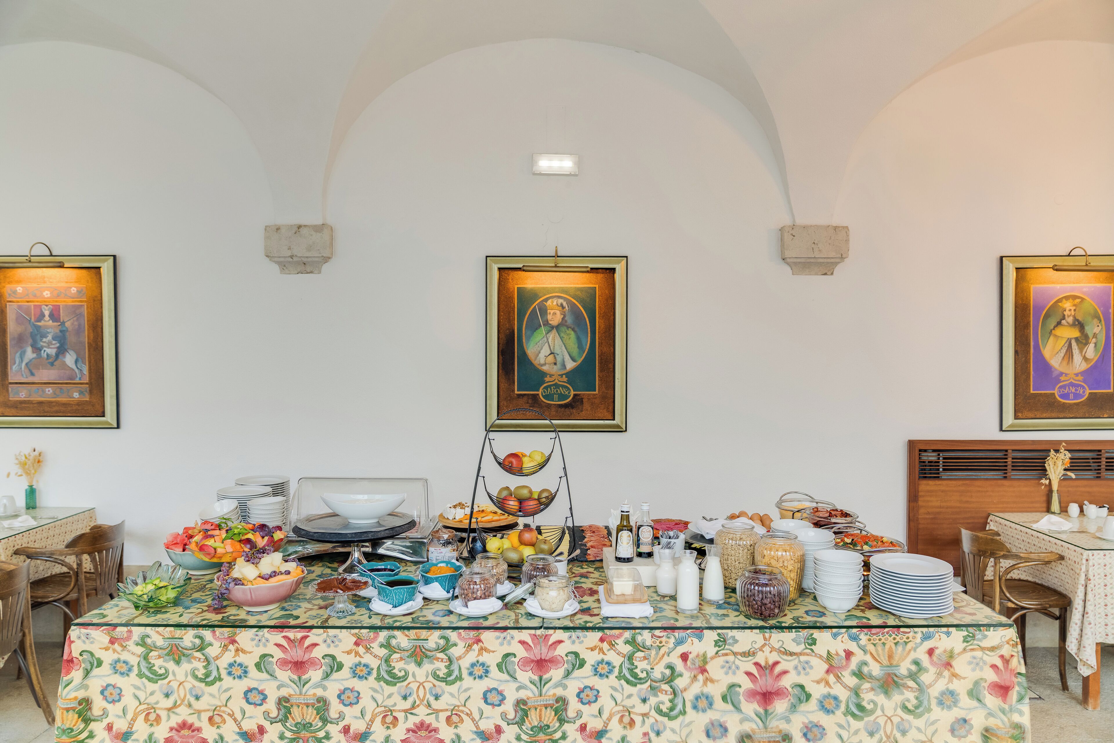 A dining area with a table set for breakfast, featuring a variety of food items and a floral tablecloth.