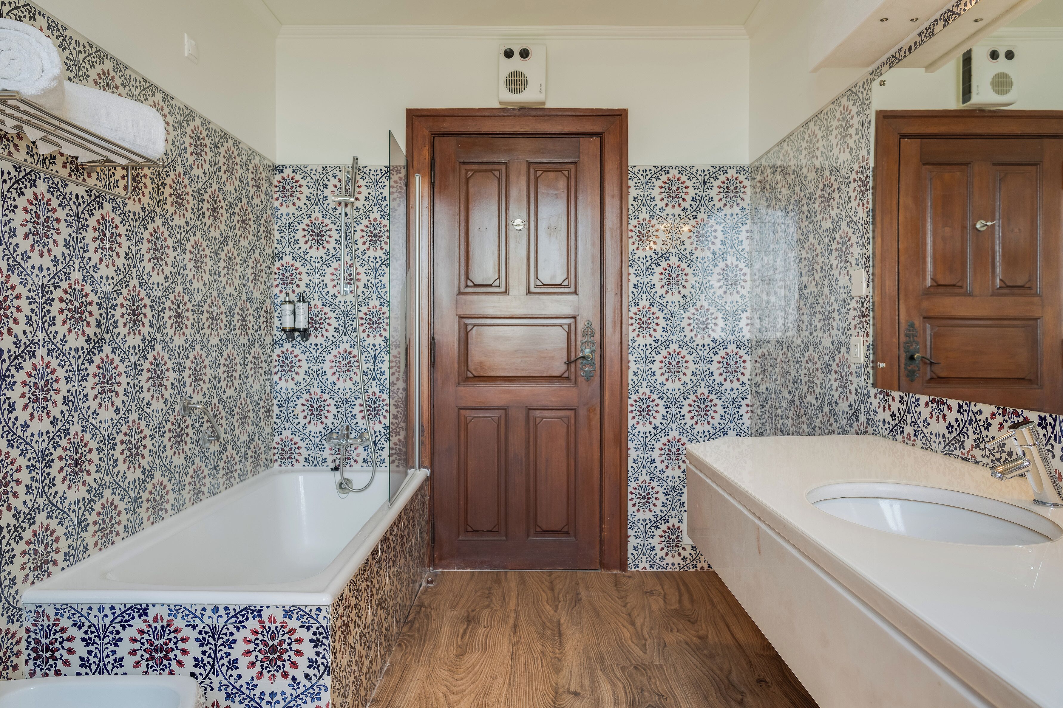 A bathroom with a wooden door, a bathtub, a sink, and patterned tiles.