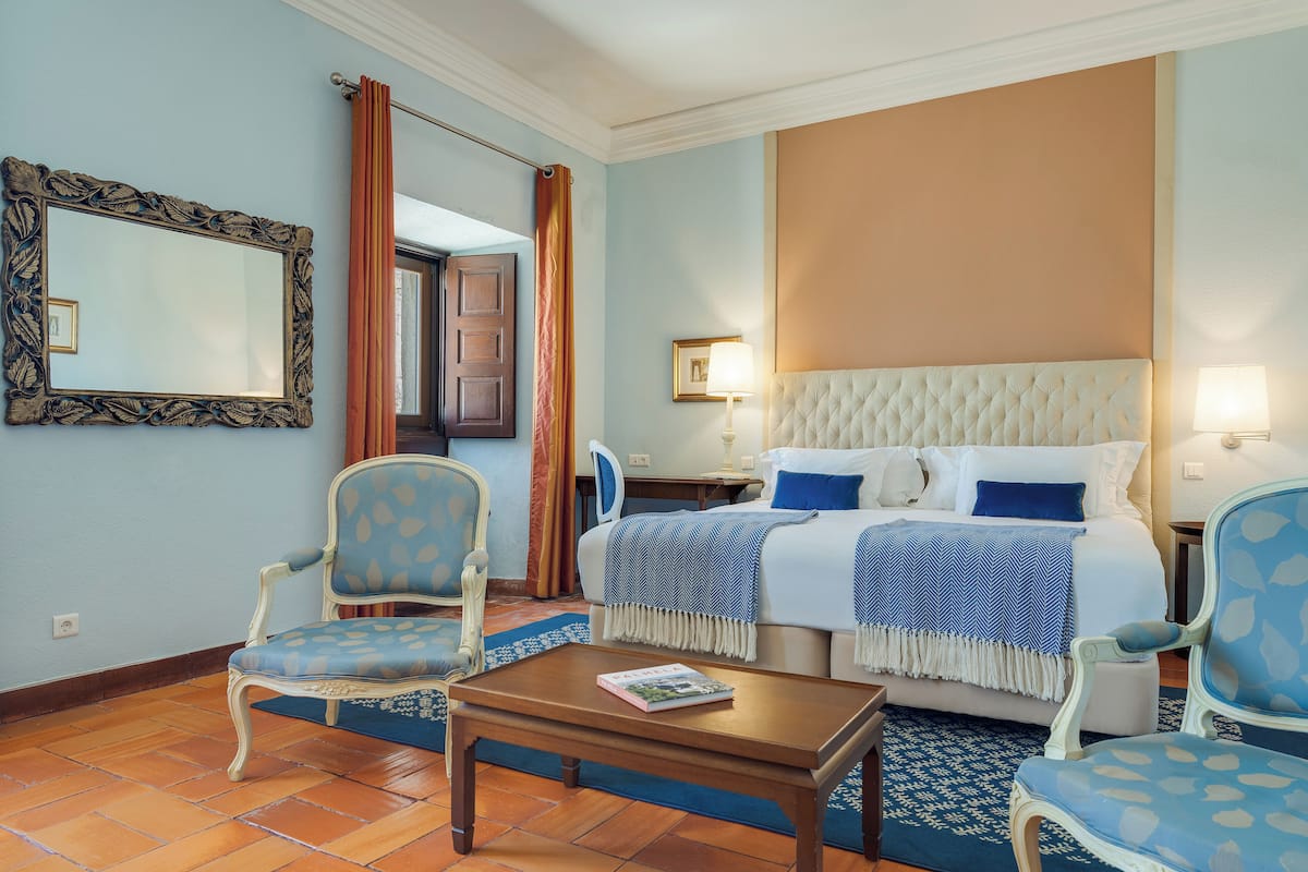 Una habitación de hotel con una cama, dos sillas, una mesa, un espejo y una lámpara.