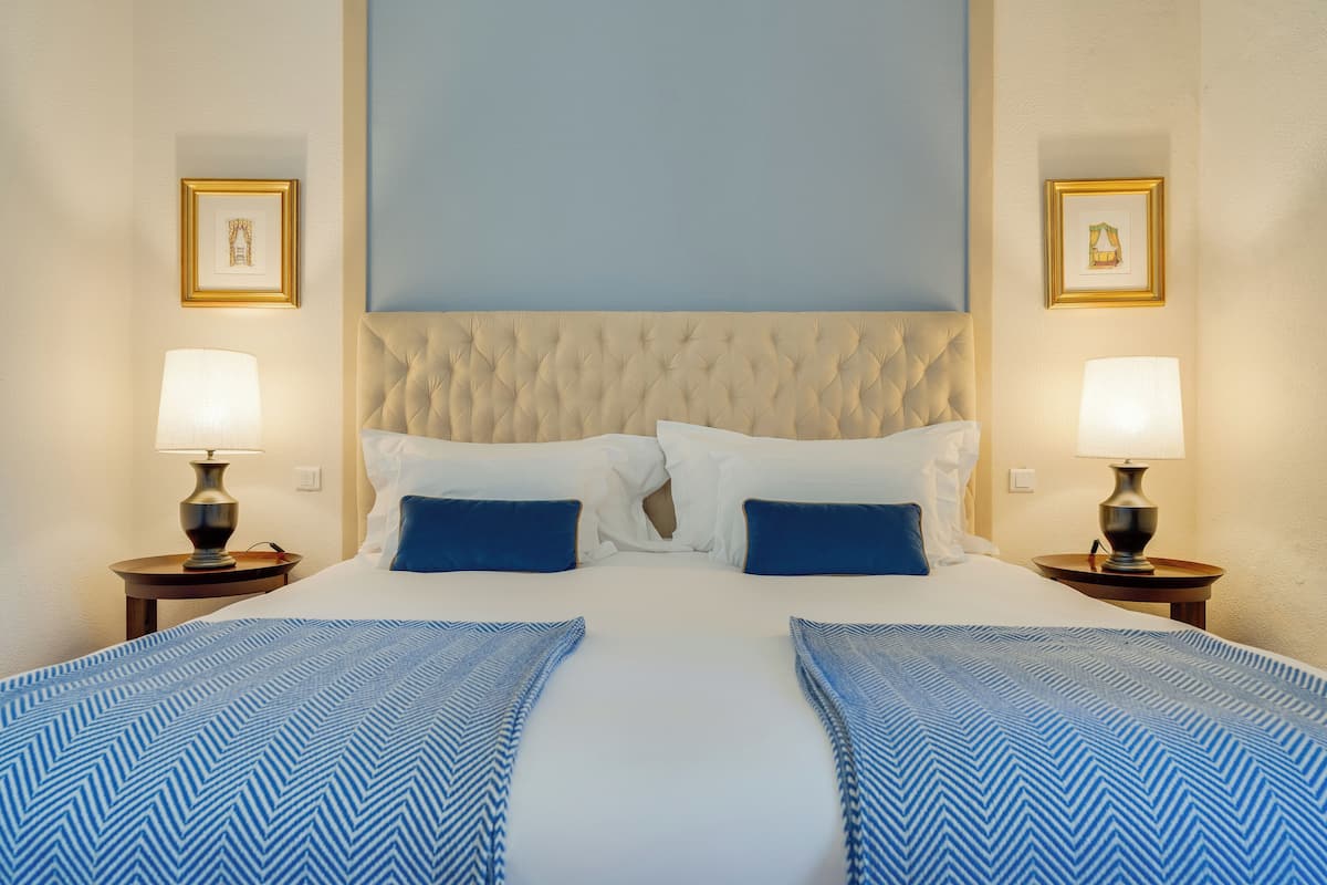 Una habitación de hotel con una cama grande, dos lámparas de noche y cuadros en las paredes.