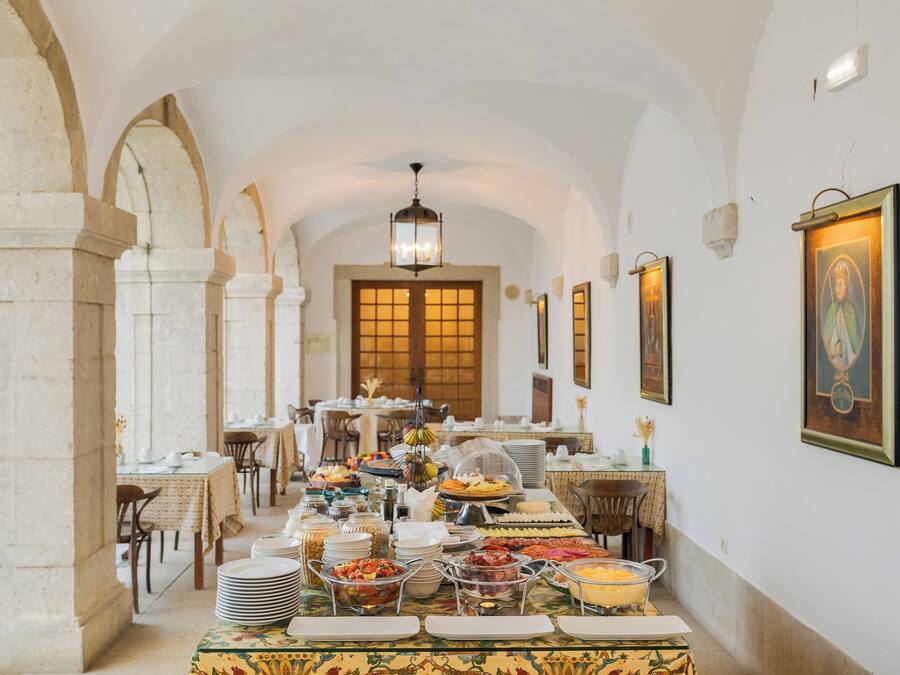 A dining hall with tables set for a meal, a chandelier, and framed artwork on the walls.