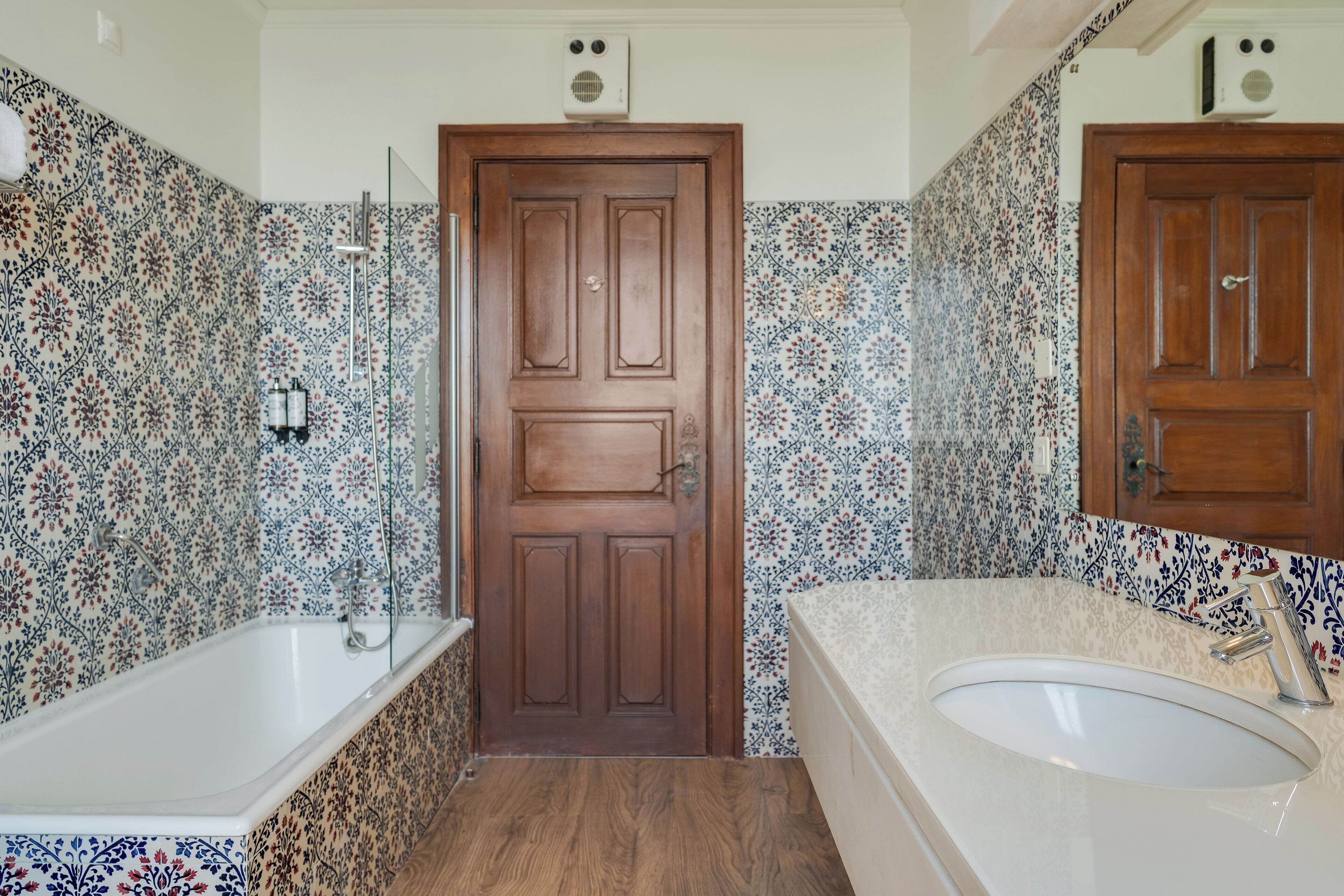A bathroom with a wooden door, a bathtub, a sink, and patterned tiles.