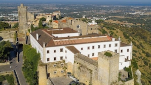 A historic building with a courtyard, surrounded by walls and a tower, overlooking a cityscape. - Pousada Castelo de Palmela - Historic Hotel (Palmela)