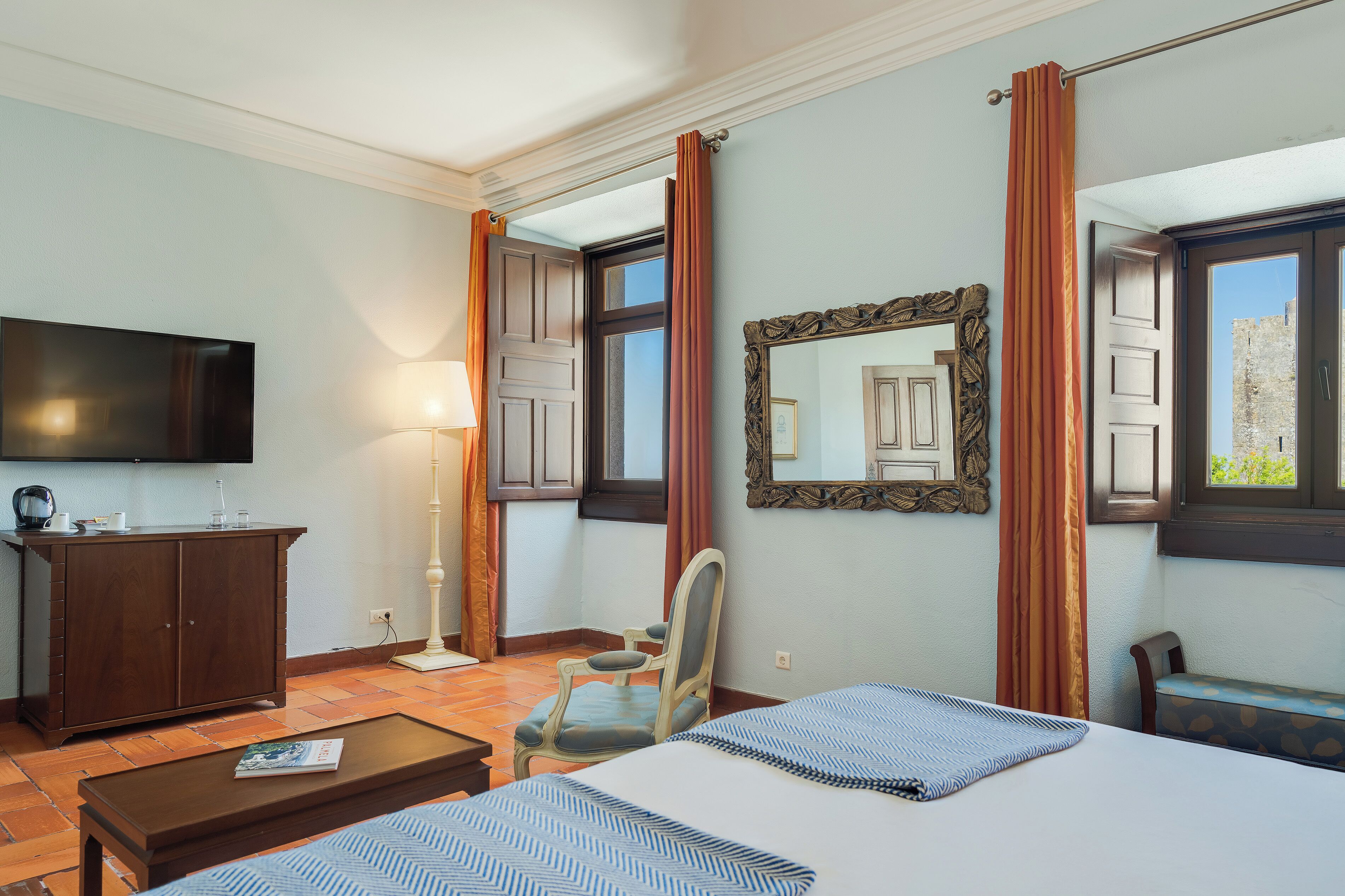 Una habitación de hotel con una cama, televisión, escritorio, silla y ventana con cortinas.