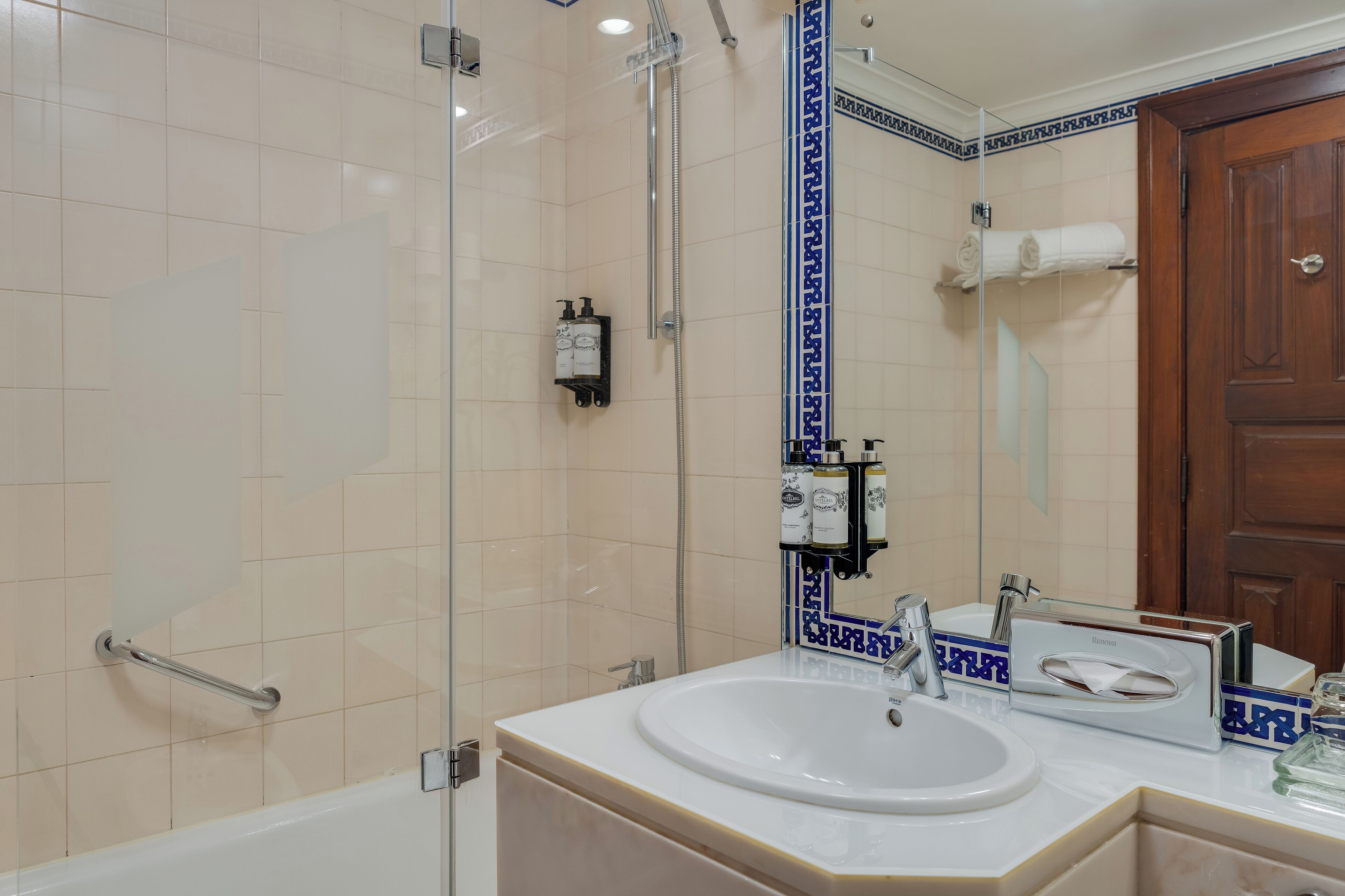 Une salle de bain avec une douche à parois de verre, un lavabo blanc avec un miroir et une porte en bois.