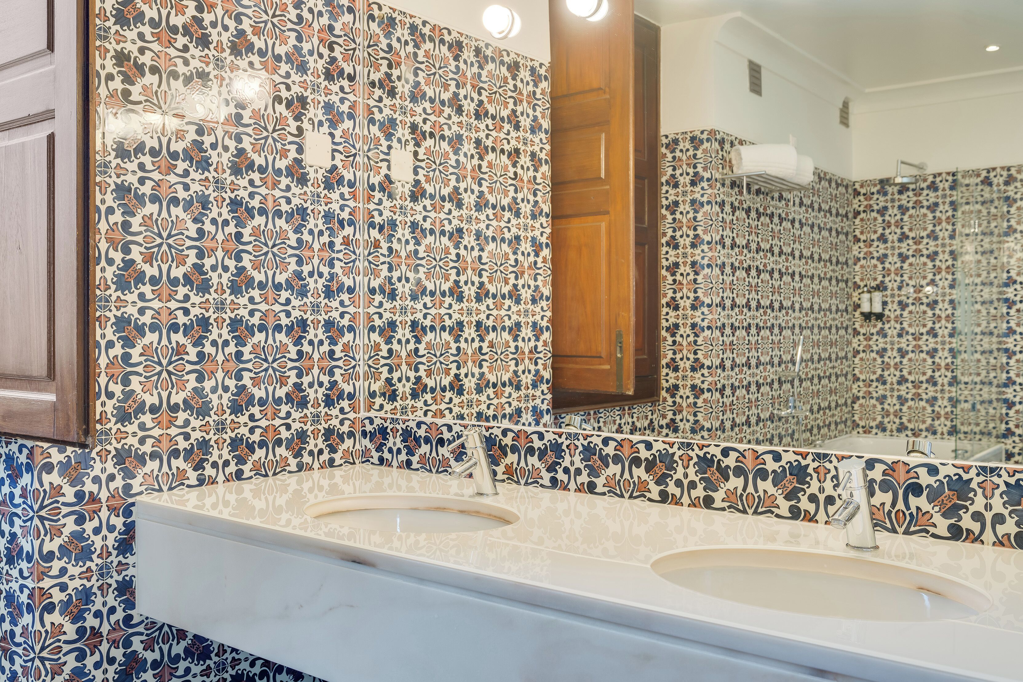 Un baño con lavamanos doble, un espejo y paredes con baldosas estampadas.