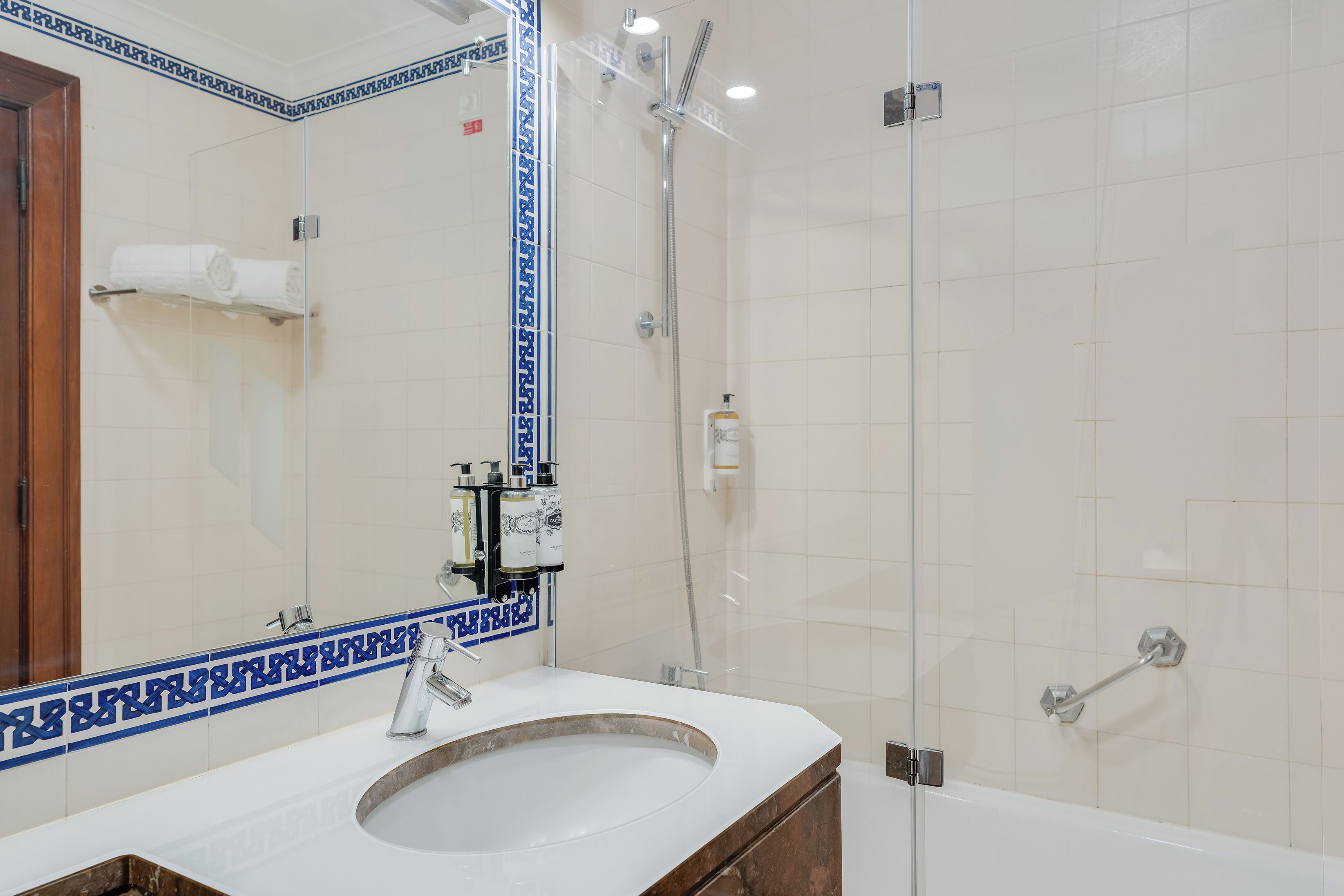A bathroom with a white sink, a glass shower enclosure, and a mirror with a blue border.